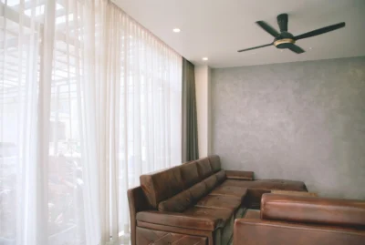 A gray-toned living room with white curtains and a black ceiling fan.