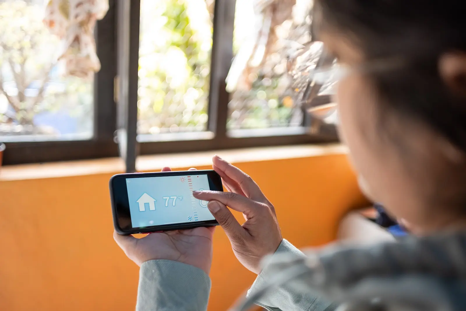 Person setting thermostat temperature to 77 degrees using a smart phone app.